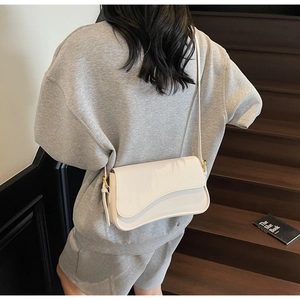 Close-up of white pebble leather crossbody bag with curved flap and gold metal hardware