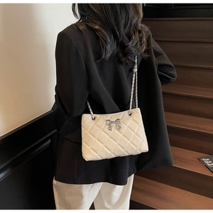 Detail of a beige quilted chain bag featuring a silver metal bow accent and chain strap
