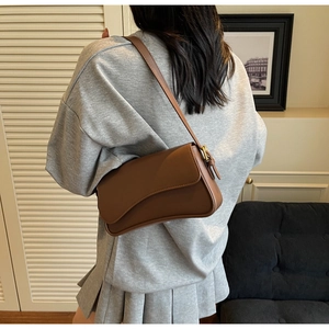 Sac baguette sous le bras en cuir marron porté à l'épaule avec un sweat-shirt gris décontracté
