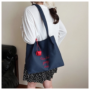 Gros plan d'un sac cabas en toile bleu marine avec broderie rouge et pendentif