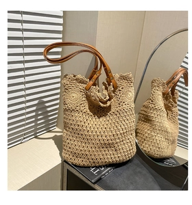Detail of hand-woven straw tote bag with brown leather handles in a cozy indoor setting