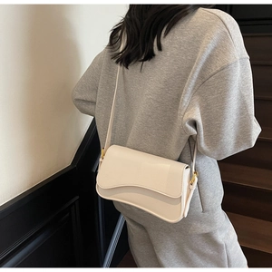 Close-up of cream crossbody bag featuring wavy flap design and gold buckle hardware