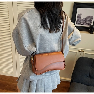 Sac à bandoulière en similicuir marron avec rabat asymétrique porté par un mannequin