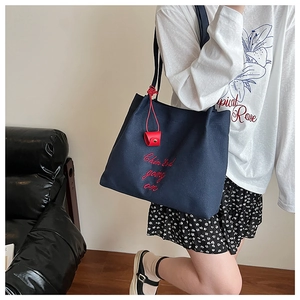 Détail du sac fourre-tout en toile bleu marine avec broderie rouge et pendentif