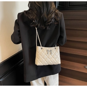 Detail of a beige quilted chain bag with a silver bow decoration worn by a model