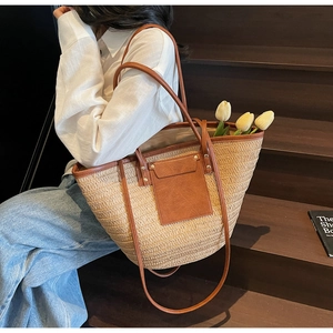 Detail of a woven straw tote bag with brown leather trim and shoulder strap for vacation