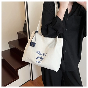 Gros plan du sac fourre-tout en toile blanche avec broderie bleue et charm carré décoratif