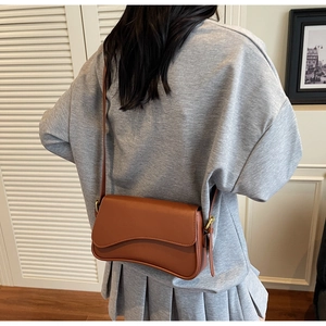 Sac à bandoulière en cuir marron réglable porté par un mannequin dans un décor épuré