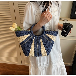 Detail of hand-woven straw tote bag with gold thread accents and round handle for resort style