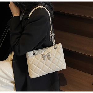Detail of quilted leather handbag with silver metal bow and chain strap on shoulder