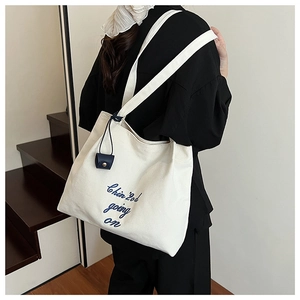 Détail du sac cabas en toile blanc cassé avec broderie bleu marine et pendentif