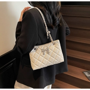 Close-up of quilted cream crossbody bag with silver bow and leather chain strap