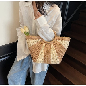 Close-up of a woven straw tote bag with fan-shaped stripes and golden chain detail