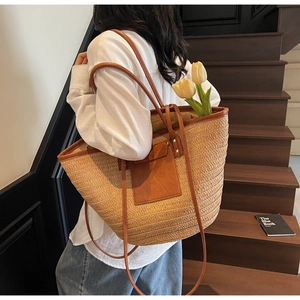 Detail of a large woven straw tote bag with brown leather accents and long shoulder straps