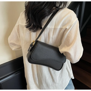 Side view of black lychee grain leather underarm bag with gold hardware on a model