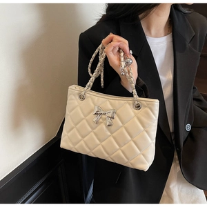 Close-up of beige quilted crossbody bag with silver bow detail worn with a black blazer