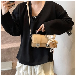 Detail of beige cylinder crossbody bag with a cute bear charm on a lifestyle staircase