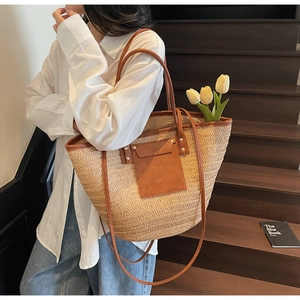 Detail view of woven straw tote bag with brown leather handles and rivet pocket accents