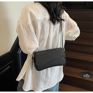 Detail of black pebbled leather texture and gold hardware on minimalist shoulder bag