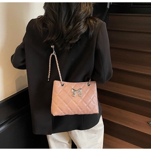 Pink quilted shoulder bag with silver bow detail worn by a model on stairs