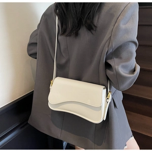 Détail du sac blanc sous le bras avec rabat ondulé et fine bandoulière sur blazer gris