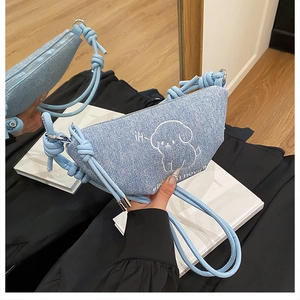 Détail du sac bandoulière en denim bleu clair avec broderie chien et bandoulières tressées