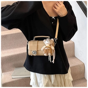 Close-up of beige glossy crossbody bag with silver clasp and cute plush bear charm