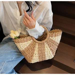 Detailed close-up of a semi-circular straw woven handbag with round handles and metal accents
