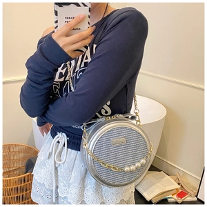 Close-up of small round crossbody bag with grey embroidery, pearls and gold chain strap