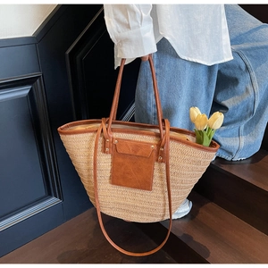 Detail of woven straw tote bag with brown leather trim and shoulder strap on a model