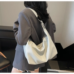 Detail of off-white pebbled leather crossbody bag on model in a minimalist office setting