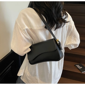 Détail d'un sac sous le bras en cuir noir avec rabat asymétrique et boucle dorée sur le côté