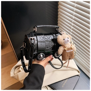 Black patent leather pillow bag with a plush bear charm held by hand in a cozy setting