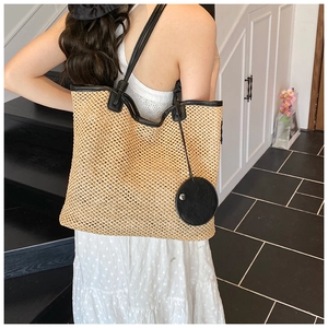 Detail of woven straw tote bag with black leather straps on a model in a polka dot dress