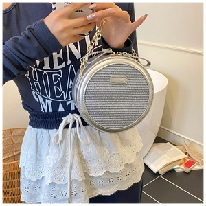 Detail of silver round crossbody bag with woven texture, metal logo and gold chain strap