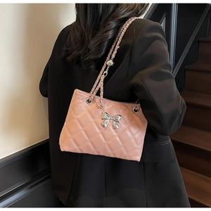 Pink quilted chain bag with silver bow buckle worn over a black blazer on shoulder