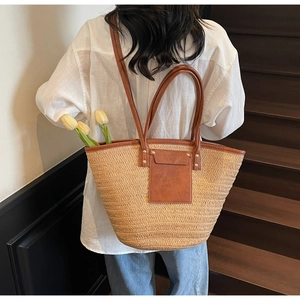 Back view of a woman wearing a large beige woven straw tote bag on wooden stairs