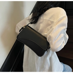 Détail du sac sous le bras en cuir noir mat avec un rabat ondulé asymétrique unique