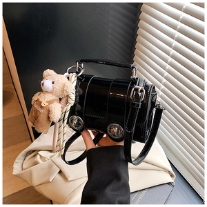 Detail of black patent leather cylinder bag with silver twist lock and plush bear charm