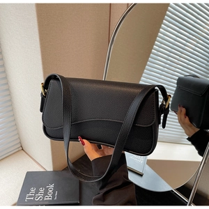 Detail view of black lychee-grain leather shoulder bag with golden buckle and light shadows