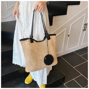 Close-up of large woven straw tote bag with black leather straps on a white dress model