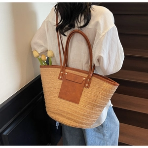 Close-up of a large woven straw tote bag with brown leather trim carried by a model