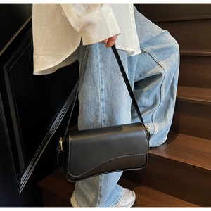 Sac sous le bras chic en cuir noir avec boucle dorée présenté dans un style urbain élégant