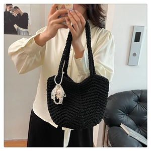Detail of black hand-woven tote bag with pearl lace charm and plush doll accessory