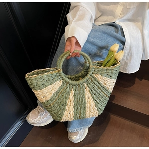 Detailed close-up of woven straw bag with green radial stripes and gold chain decor