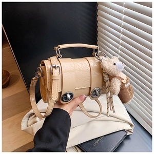 Detail of light brown patent leather pillow bag with silver locks and teddy bear charm
