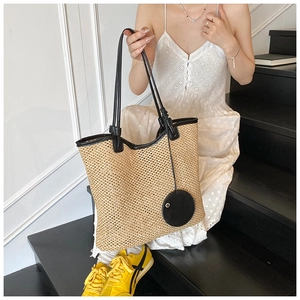 Detail of woven straw tote bag with black leather handle and round decorative charm