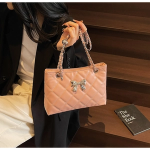 Detail of pink quilted handbag with silver bow ornament and chain strap held by model