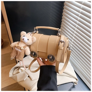 Detail shot of beige structured pillow bag with silver buckles and a cute plush bear charm