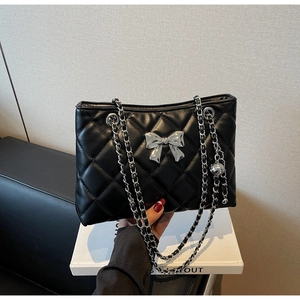 Detail of black quilted leather bag with silver bow ornament and chain strap